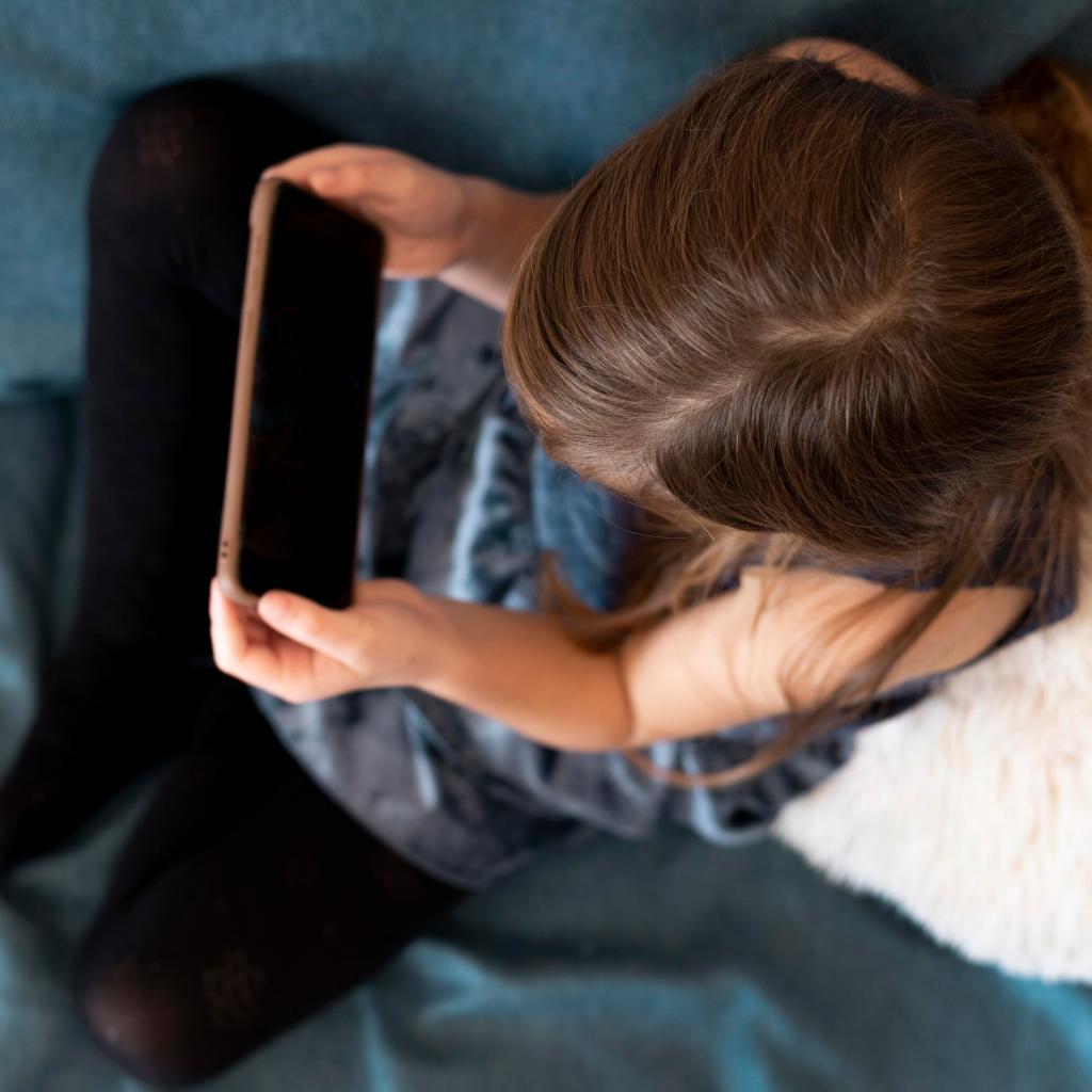 Little girl using her smartphone in bed